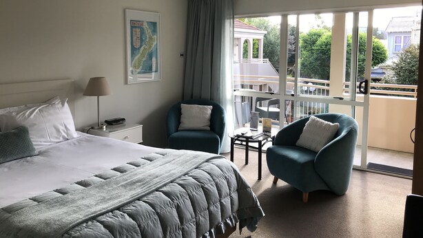 A hotel room with a bed, a chair, a small table, and a balcony with a view of the outside. - Tuscana Motor Lodge (Christchurch)