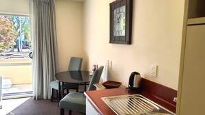 A small kitchenette with a sink, a table with chairs, a clock on the wall, and a view of the outside. - Tuscana Motor Lodge (Christchurch)
