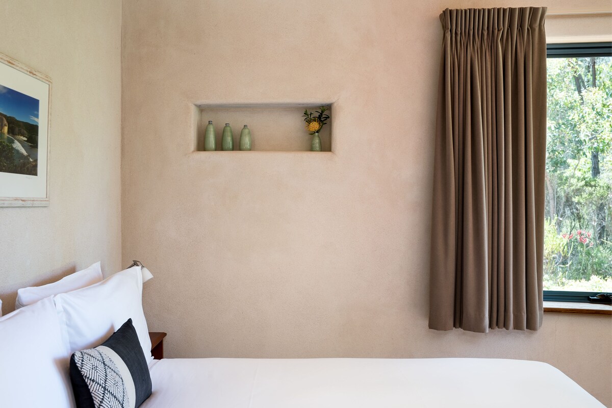 Ein Schlafzimmer mit einem Bett, Kissen, einer Ablage mit Vasen und einem Fenster mit Vorhängen.