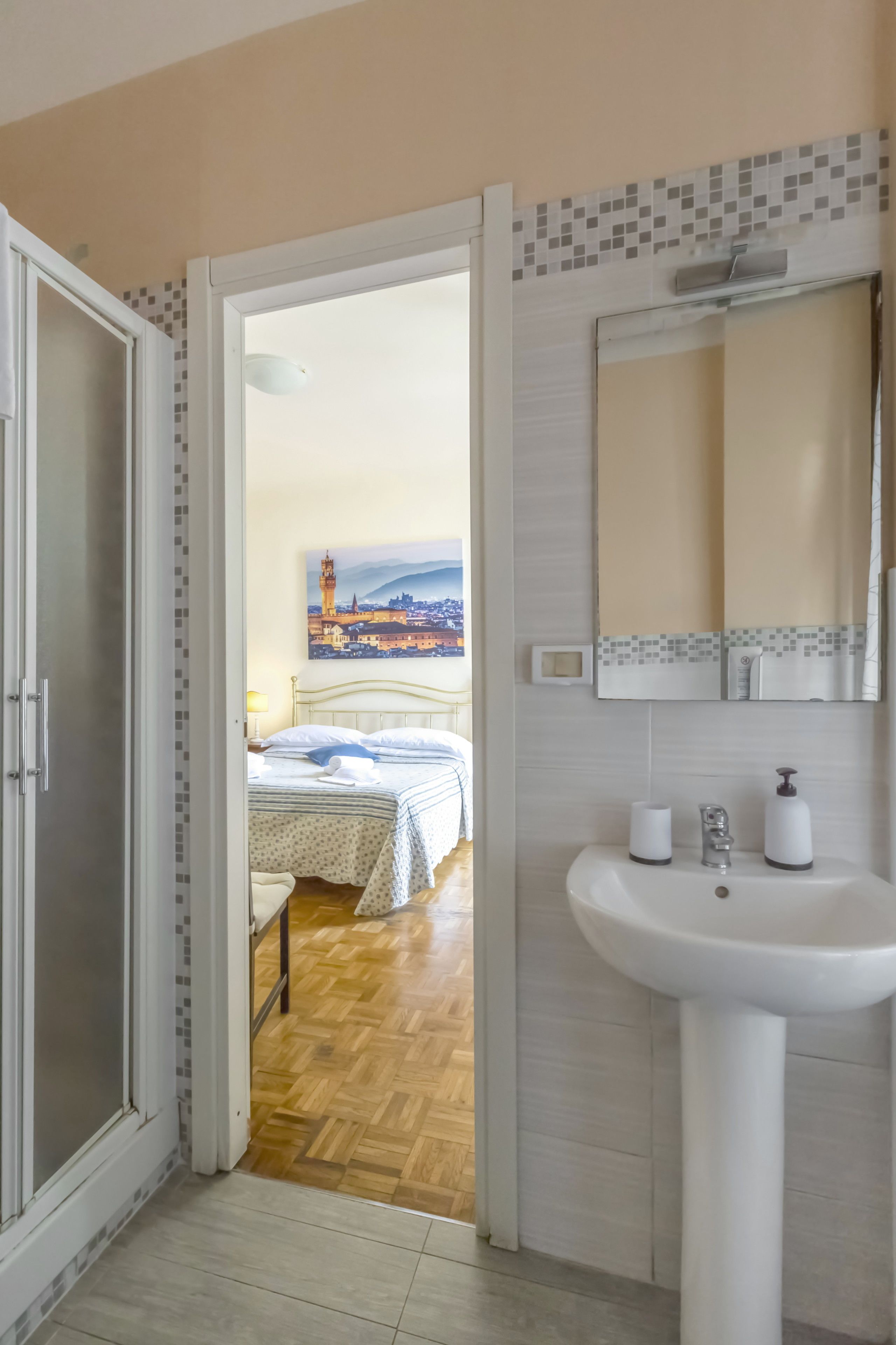 Une chambre d’hôtel avec un lit, une salle de bain comprenant un lavabo et un miroir, et un couloir menant à une autre pièce.