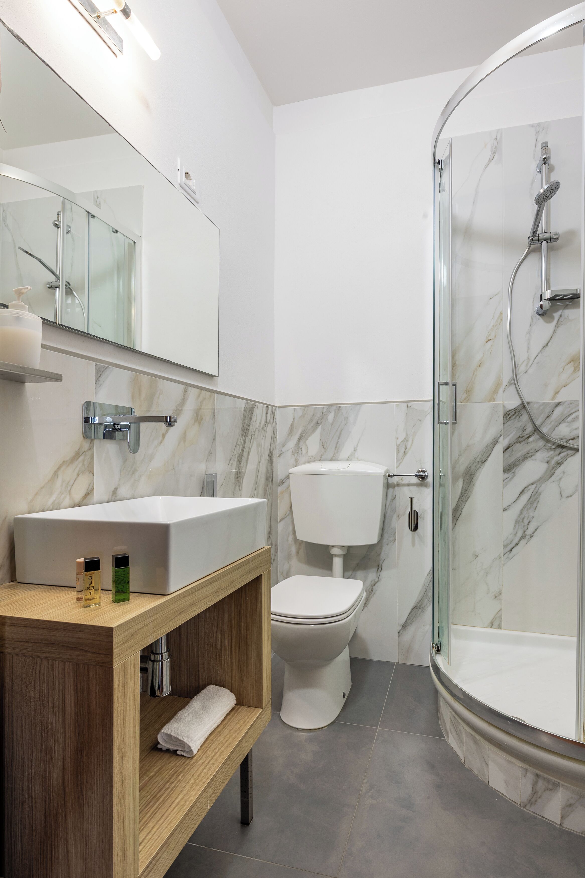 A modern bathroom with a marble vanity, a glass-enclosed shower, and a toilet.