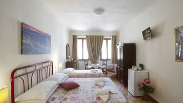 A hotel room with two beds, a desk, a chair, a small table, a refrigerator, and a window with curtains.