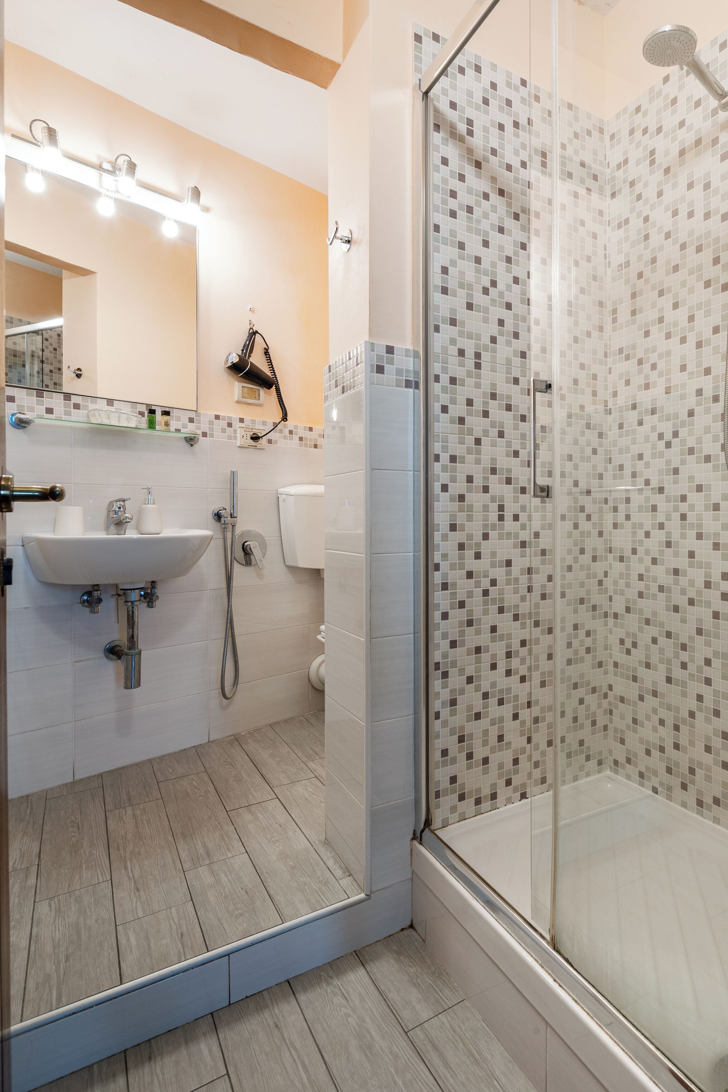 Un baño con ducha de vidrio, lavamanos con espejo y piso de baldosas.