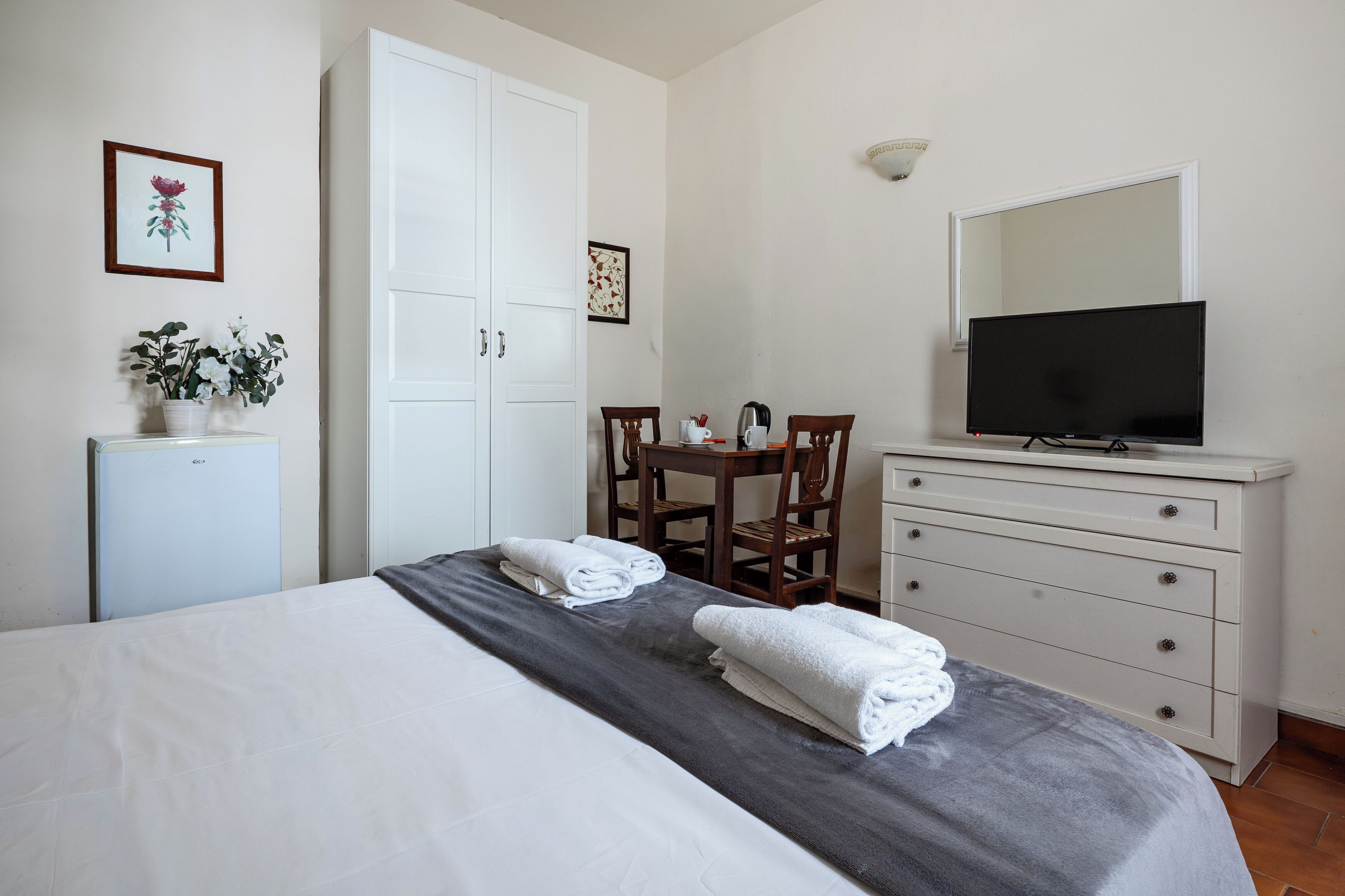 A bedroom with a bed, a desk with a chair, a television, a dresser, and a small refrigerator.