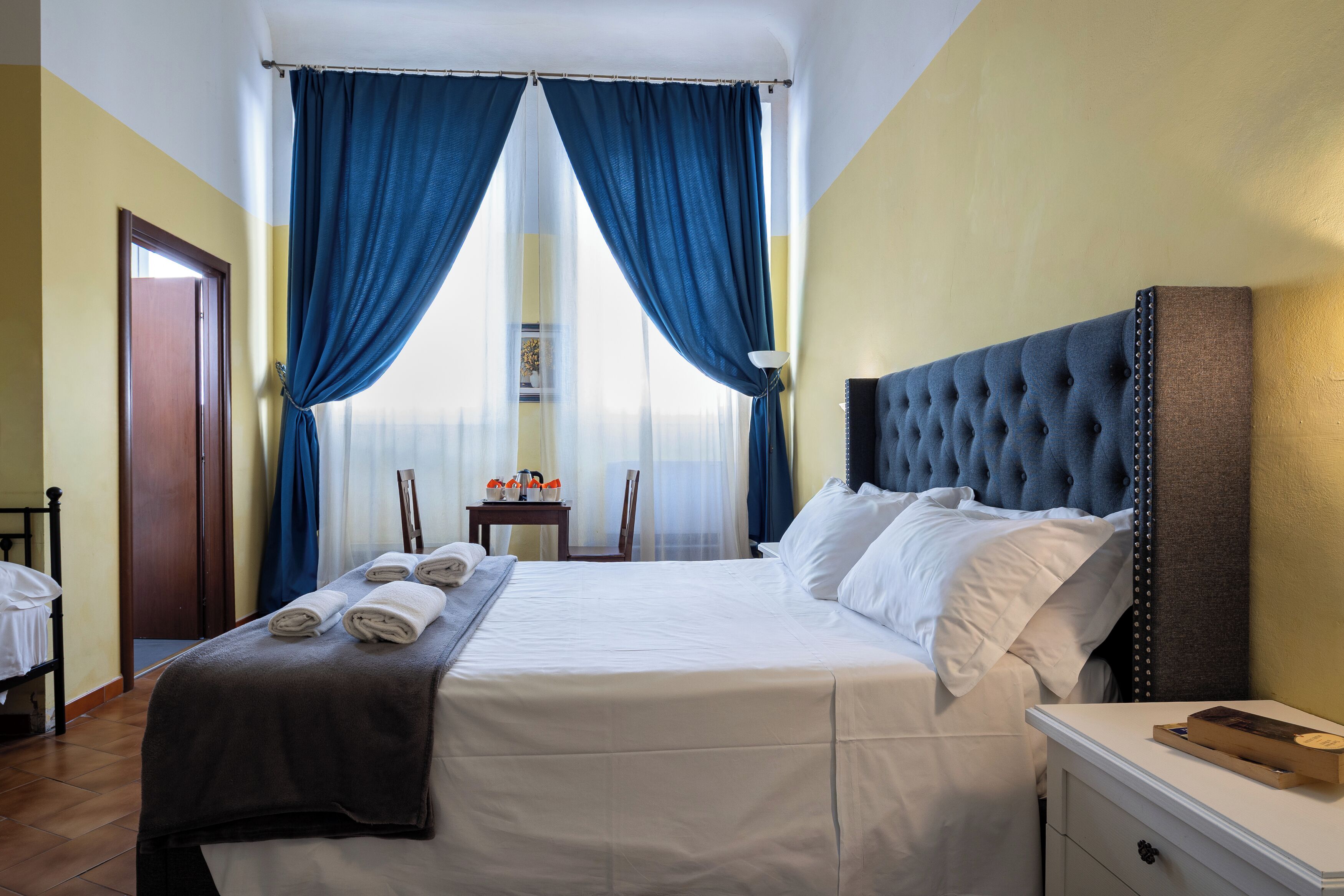 A neatly made bed with white linens, a dark headboard, and blue curtains.