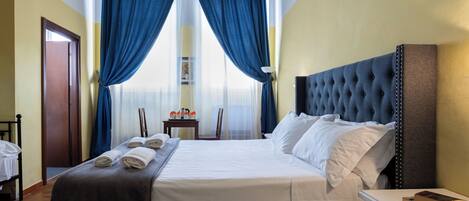 A neatly made bed with white linens, a dark headboard, and blue curtains.