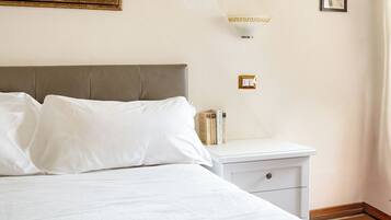 Un lit bien fait, avec du linge de lit blanc, une table de chevet avec une lampe et un tableau encadré au mur.