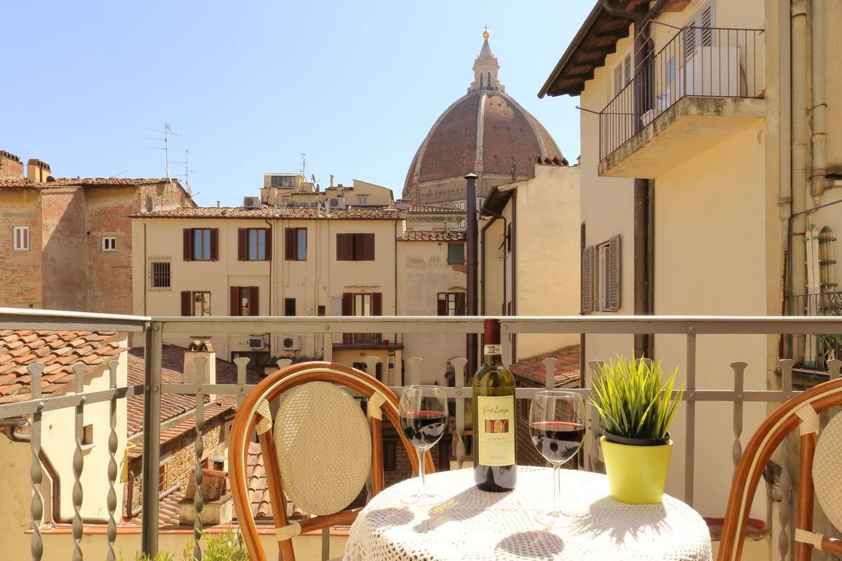 A balcony with a table, chairs, a bottle of wine, and a potted plant.