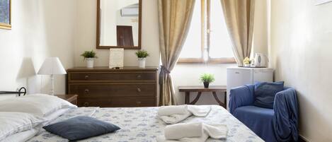 A hotel room with a bed, a dresser, a desk, a chair, and a window with curtains.