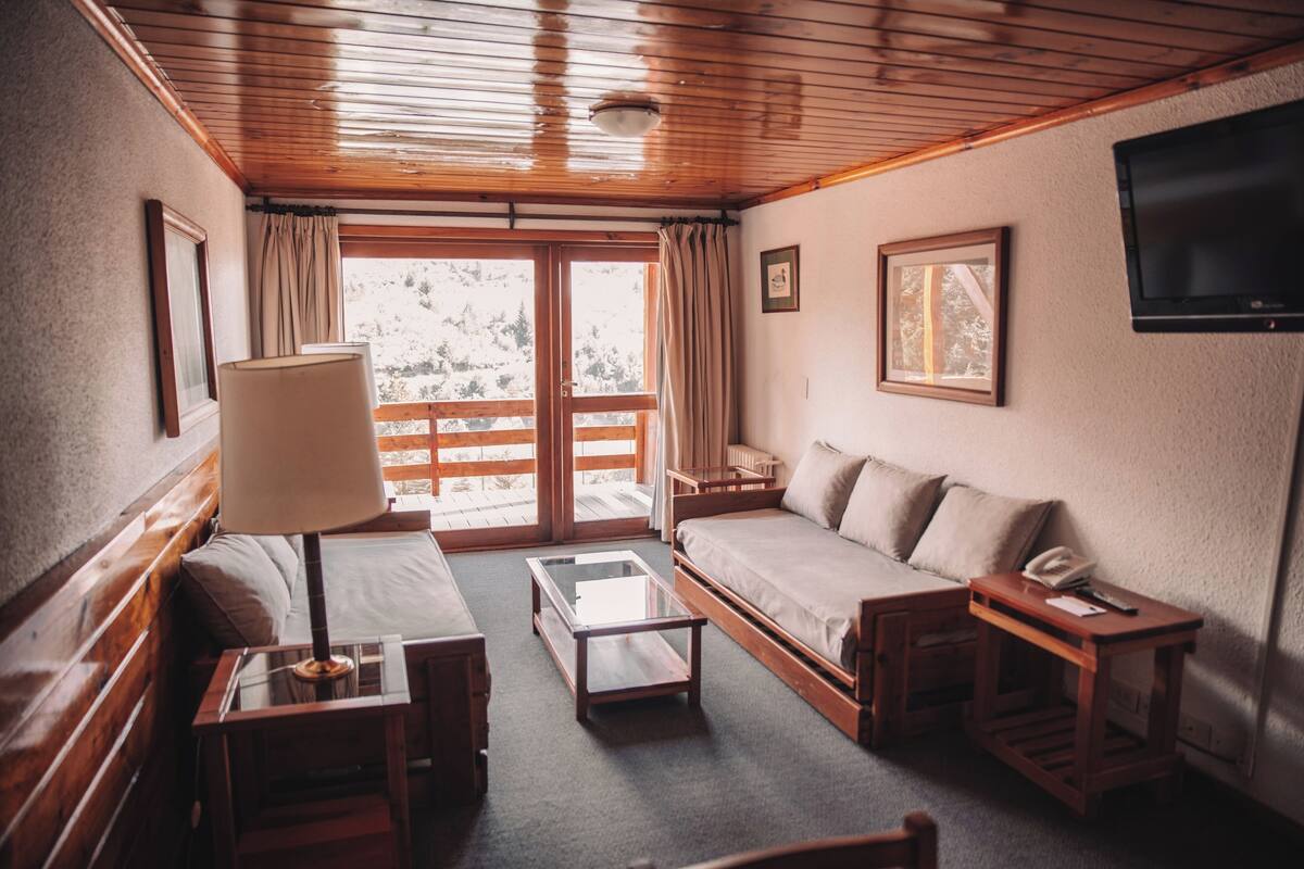 Ein gemütliches Zimmer mit Holzbalkendecke, einer Couch, einem kleinen Tisch und einem an der Wand befestigten Fernseher.