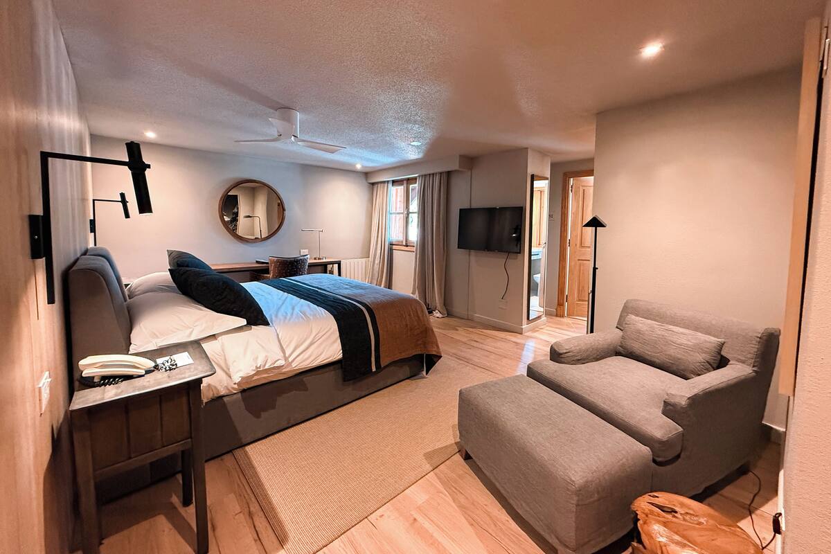 Ein modernes Hotelzimmer mit Bett, Nachttisch, Lampe, Stuhl und einem an der Wand befestigten Fernseher.