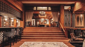 A grand wooden staircase leading to a living area with a chandelier, wooden walls, and a patterned rug. - Hotel Catedral Patagonia Ski & Wellness (San Carlos de Bariloche)