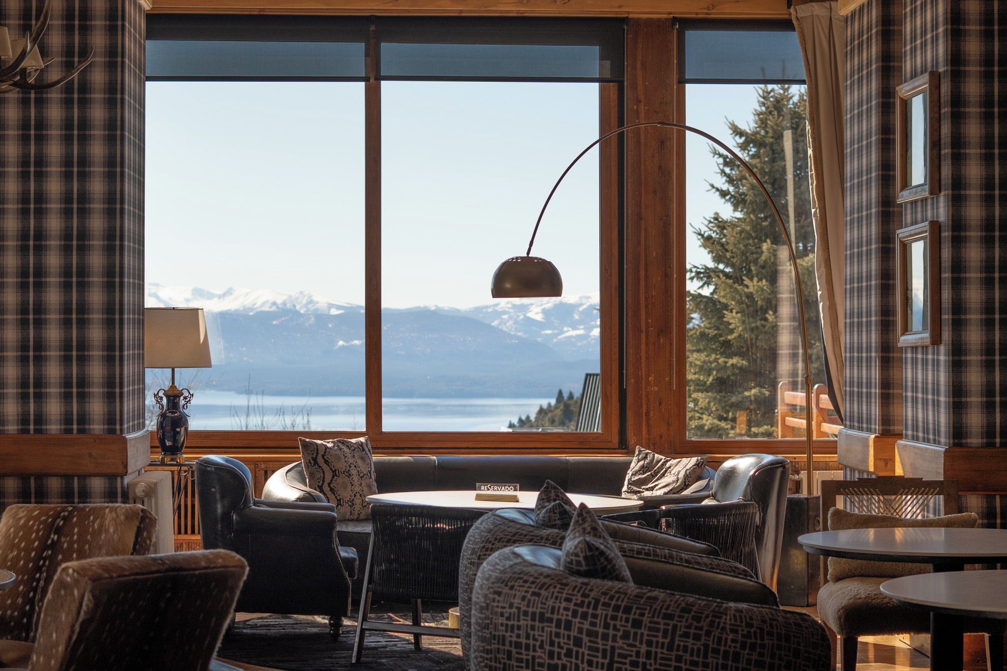 A cozy room with a large window offering a mountain view, a table with chairs, and a lamp.