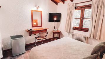 Un dormitorio con techo de madera, una cama con colcha, un escritorio con silla, un televisor y una ventana con cortinas.