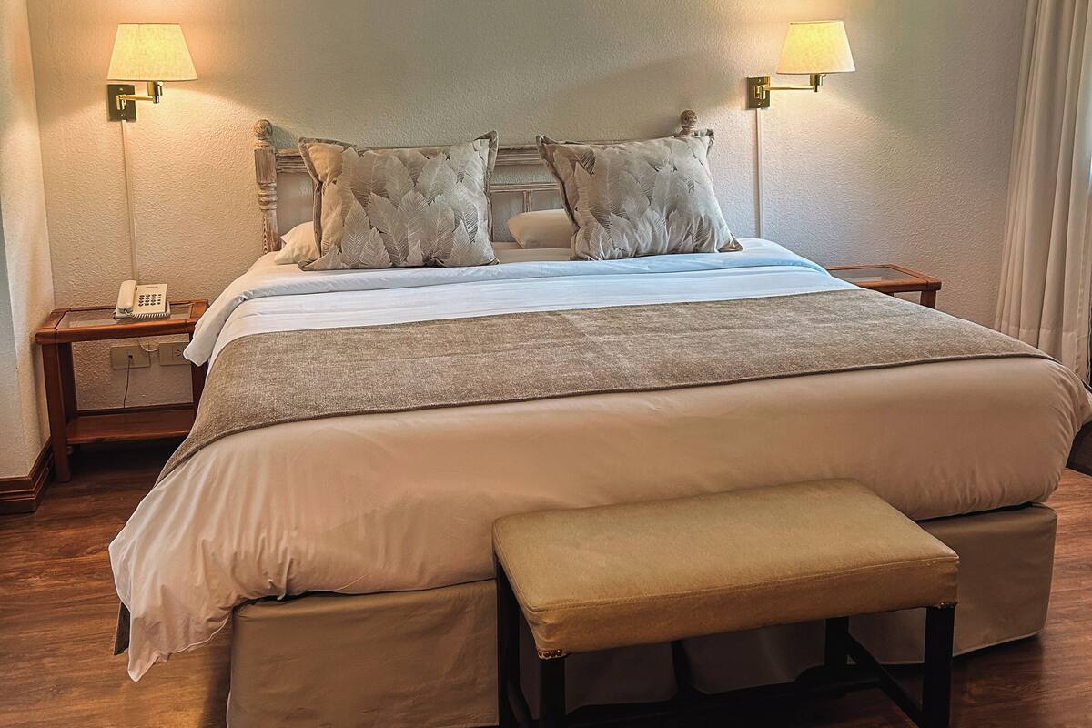 Ein Schlafzimmer mit einem großen Bett, zwei Nachttischlampen, einem Telefon am Nachttisch und einer hölzernen Bank.
