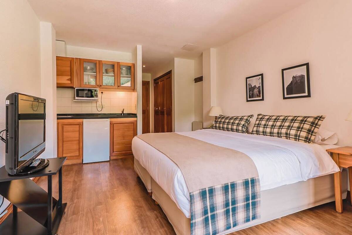 Ein Schlafzimmer mit Bett, Fernseher auf einem Schrank, einer Küchenzeile mit Schränken und einer Mikrowelle.