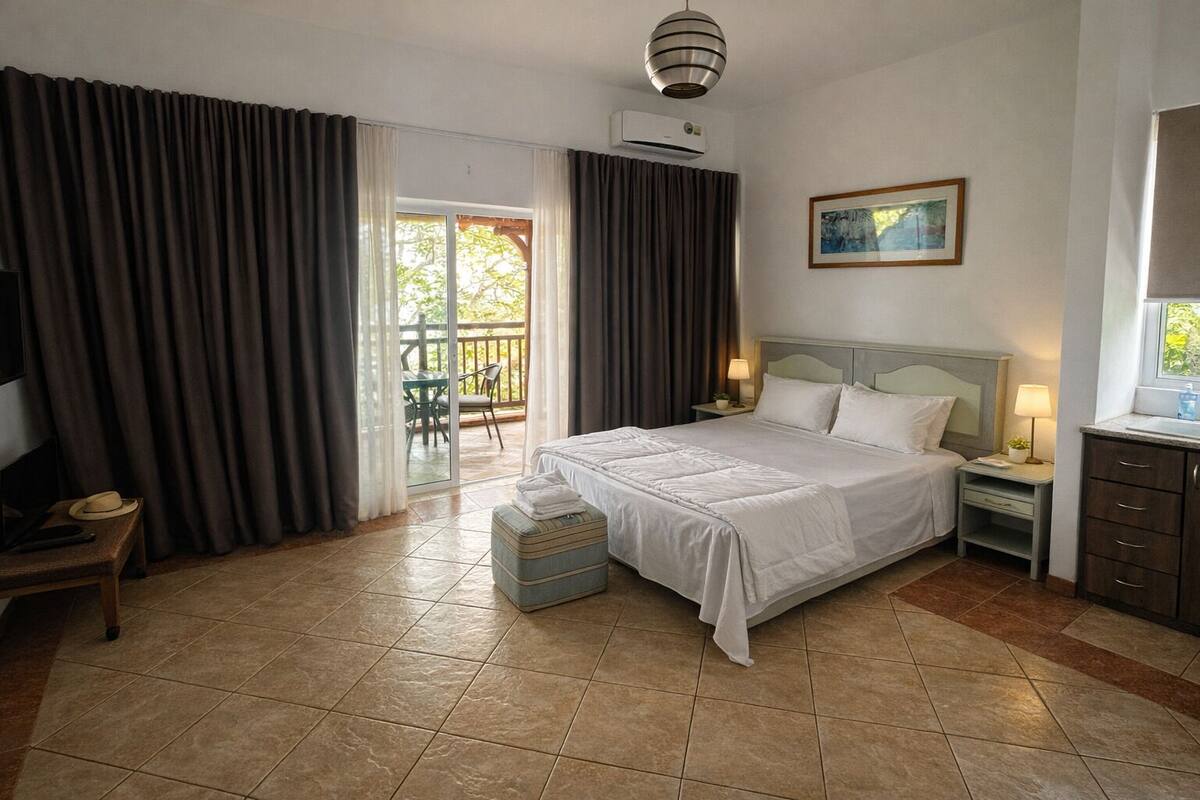A hotel room with a bed, a TV, a desk, and a balcony with curtains.