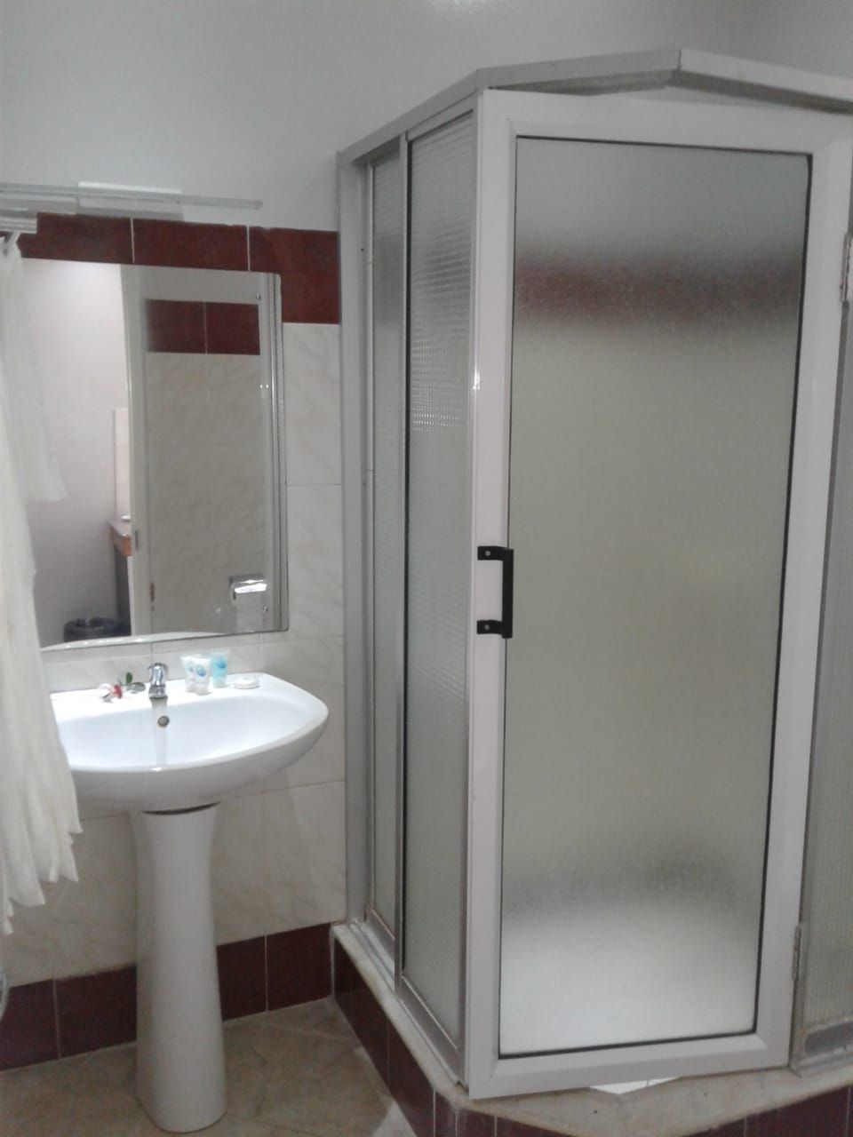 A bathroom with a white pedestal sink, a mirror, and a frosted glass shower enclosure.