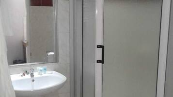 A bathroom with a white pedestal sink, a mirror, and a frosted glass shower enclosure.