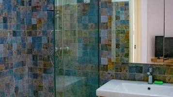 Un bagno con doccia vetro, pareti piastrellate, un mobile lavabo in legno e uno specchio sopra il lavello.