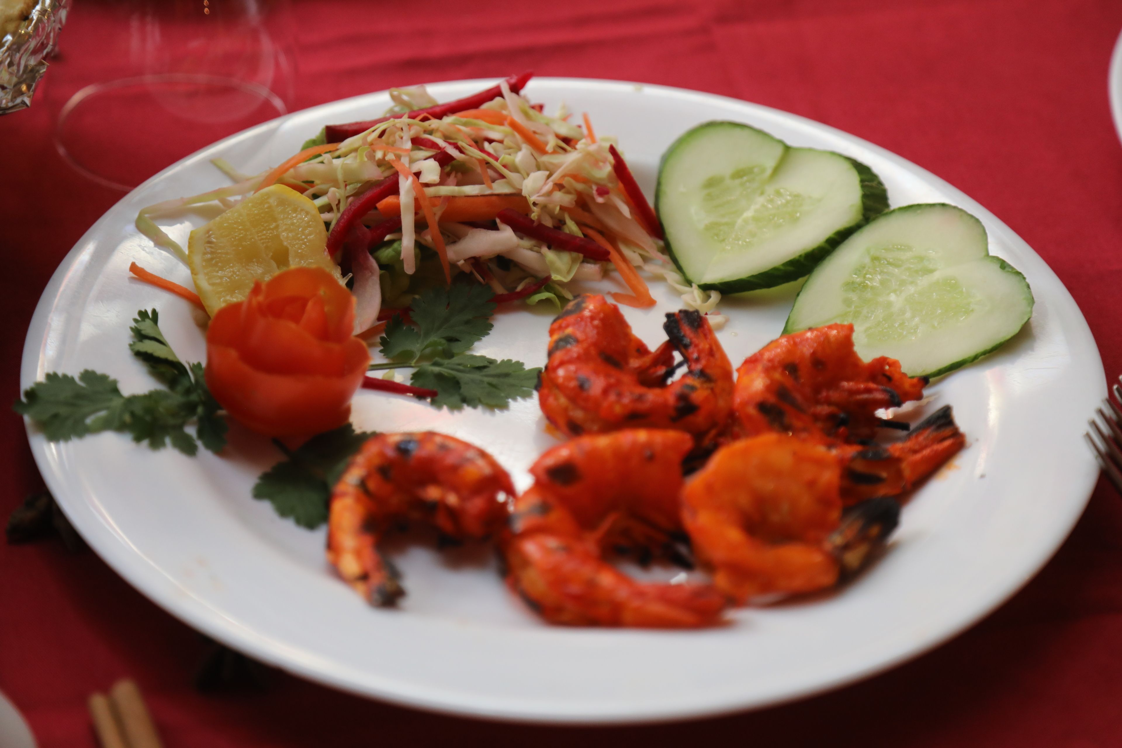 A plate of grilled shrimp, cucumber slices, and a carrot salad on a white plate.