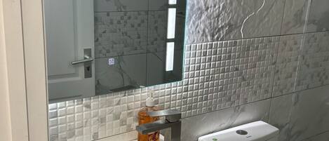 A bathroom with a white sink, a mirror, a toilet, and a glass partition.