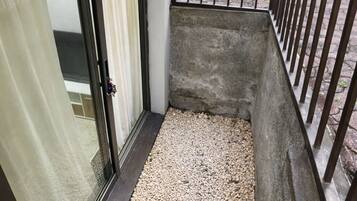 A narrow outdoor space with a gravel floor, a metal railing, and a sliding glass door leading to a balcony.