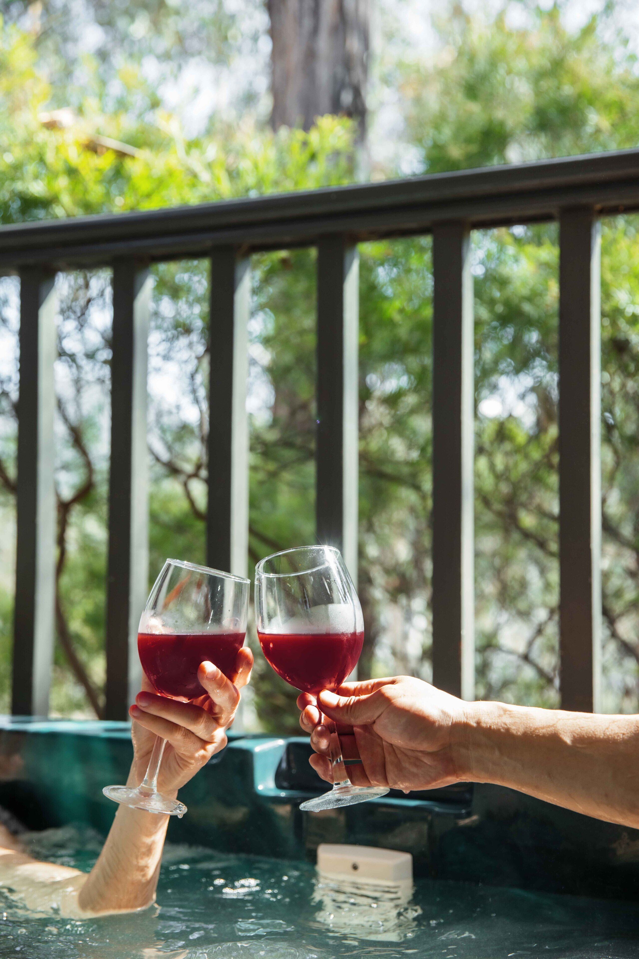 Deux mains tenant des verres de vin, avec un jacuzzi en arrière-plan.