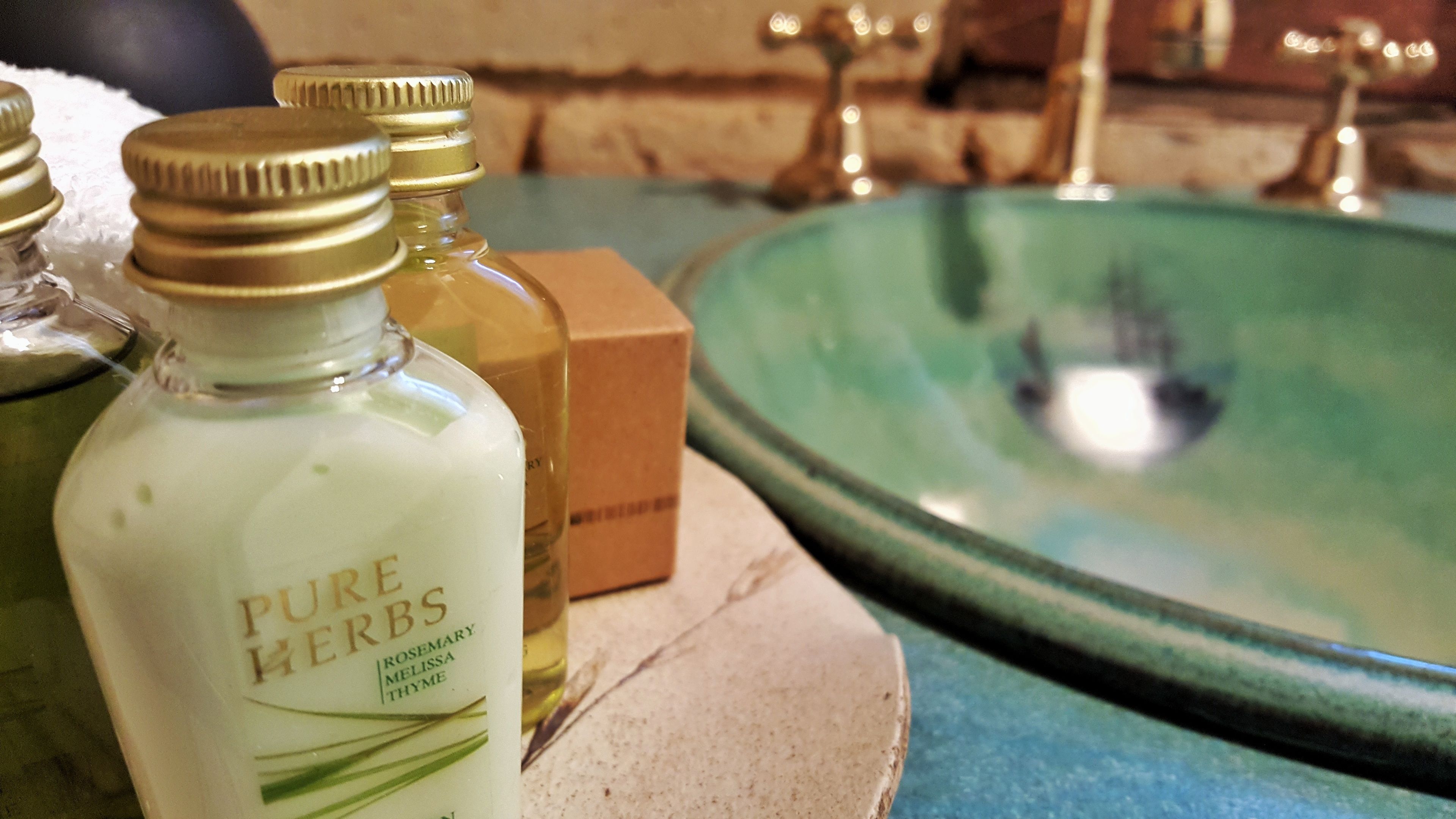 A bathroom with a green sink, a bottle of Pure Herbs, and a box of toiletries.