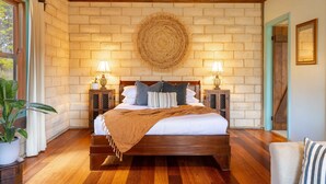 Ein Schlafzimmer mit einem hölzernen Bett, zwei Nachttischen mit Lampen, einem großen Wandteppich und einer Topfpflanze.