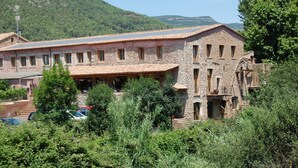 A stone building with multiple windows and a tiled roof, surrounded by greenery and a hilly landscape. - Hotel Molí de la Torre (Bigues I Riells)