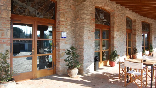 A stone building with large arched windows and a wooden door. There are potted plants and outdoor seating. - Hotel Molí de la Torre (Bigues I Riells)