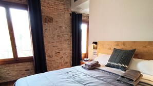 A bedroom with a large bed, a wooden headboard, and a brick wall. - Hotel Molí de la Torre (Bigues I Riells)
