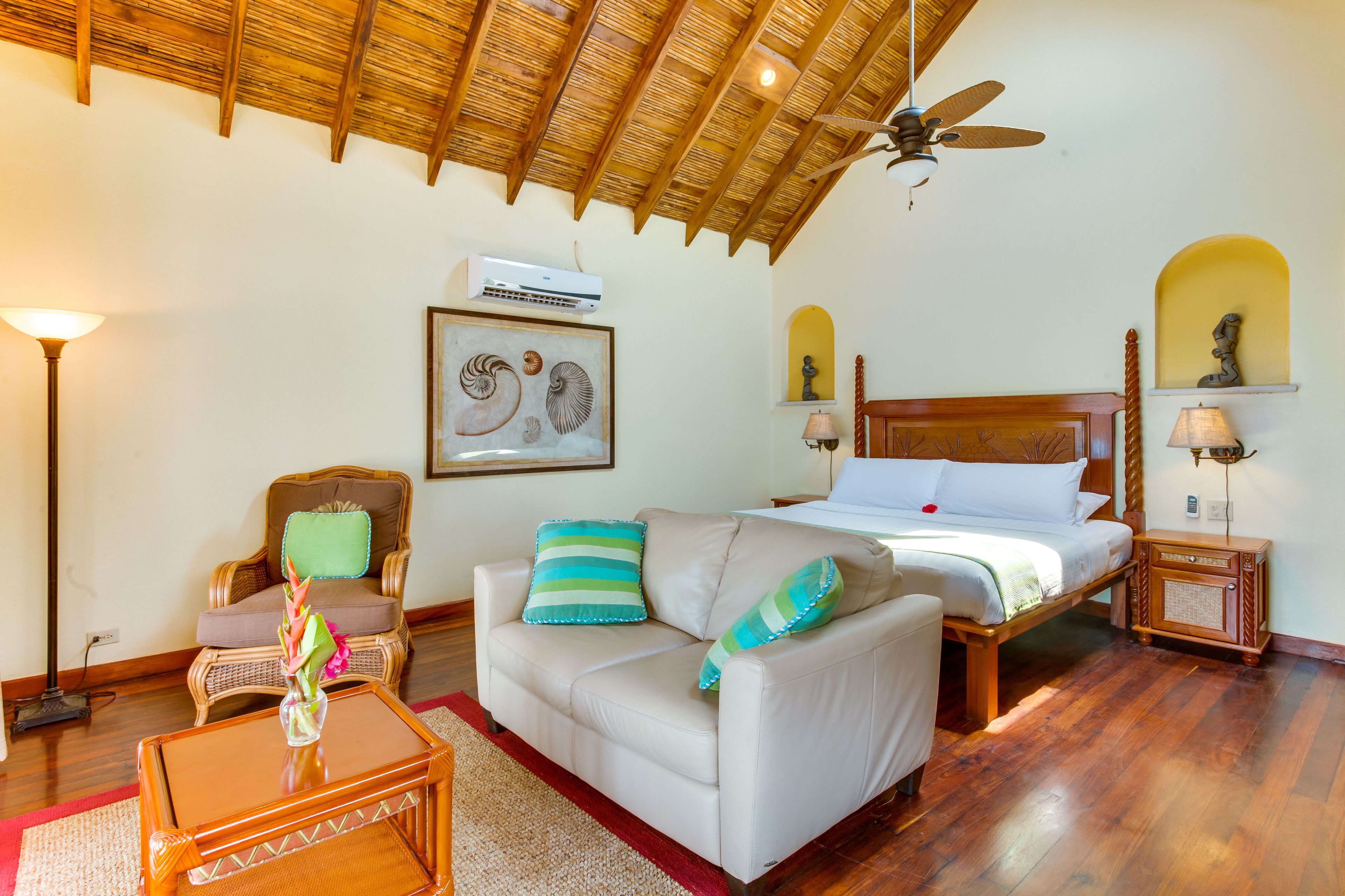 A well-lit bedroom with a bed, a sofa, a chair, a coffee table, and a ceiling fan.