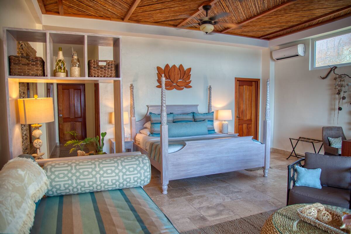 A spacious bedroom with a large bed, a sitting area with a sofa, and a wooden ceiling.