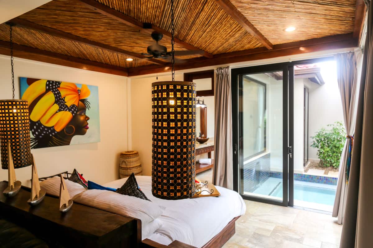 A bedroom with a bed, a ceiling fan, a painting, and a view of a pool through a glass door.