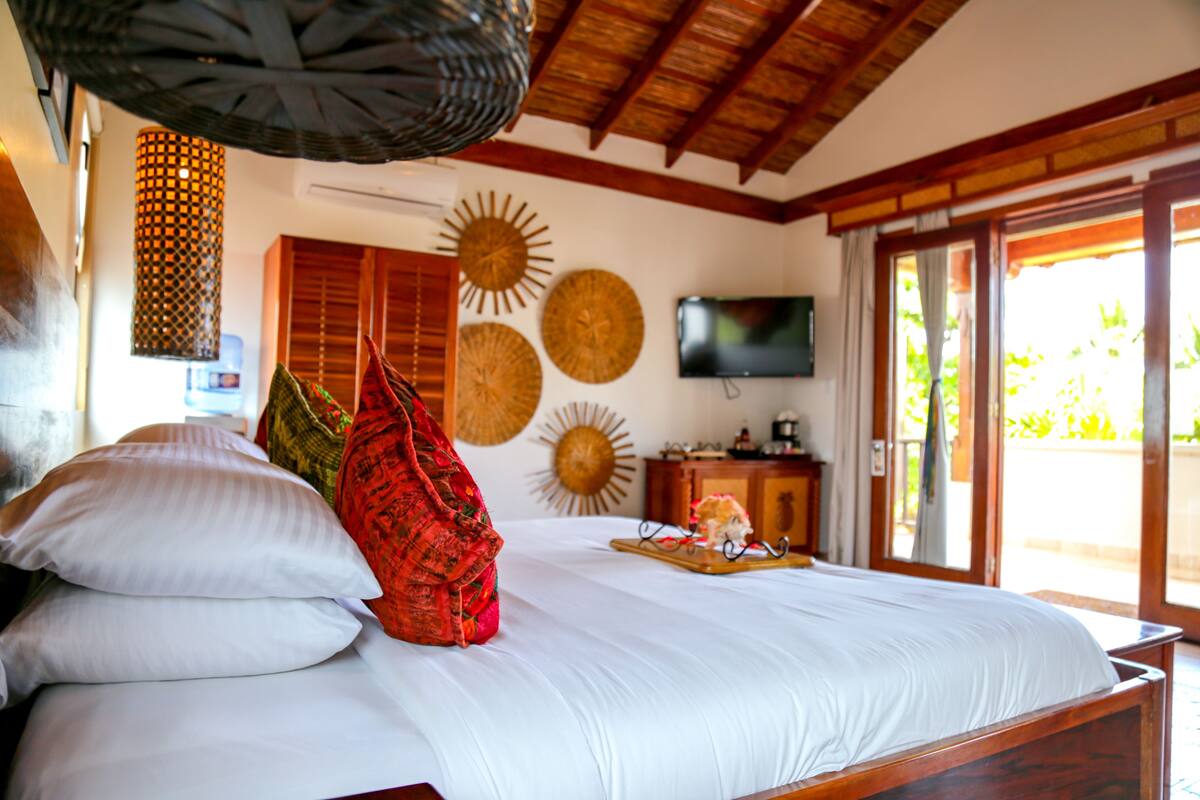 A bedroom with a large bed, a television, and a view of the outdoors.