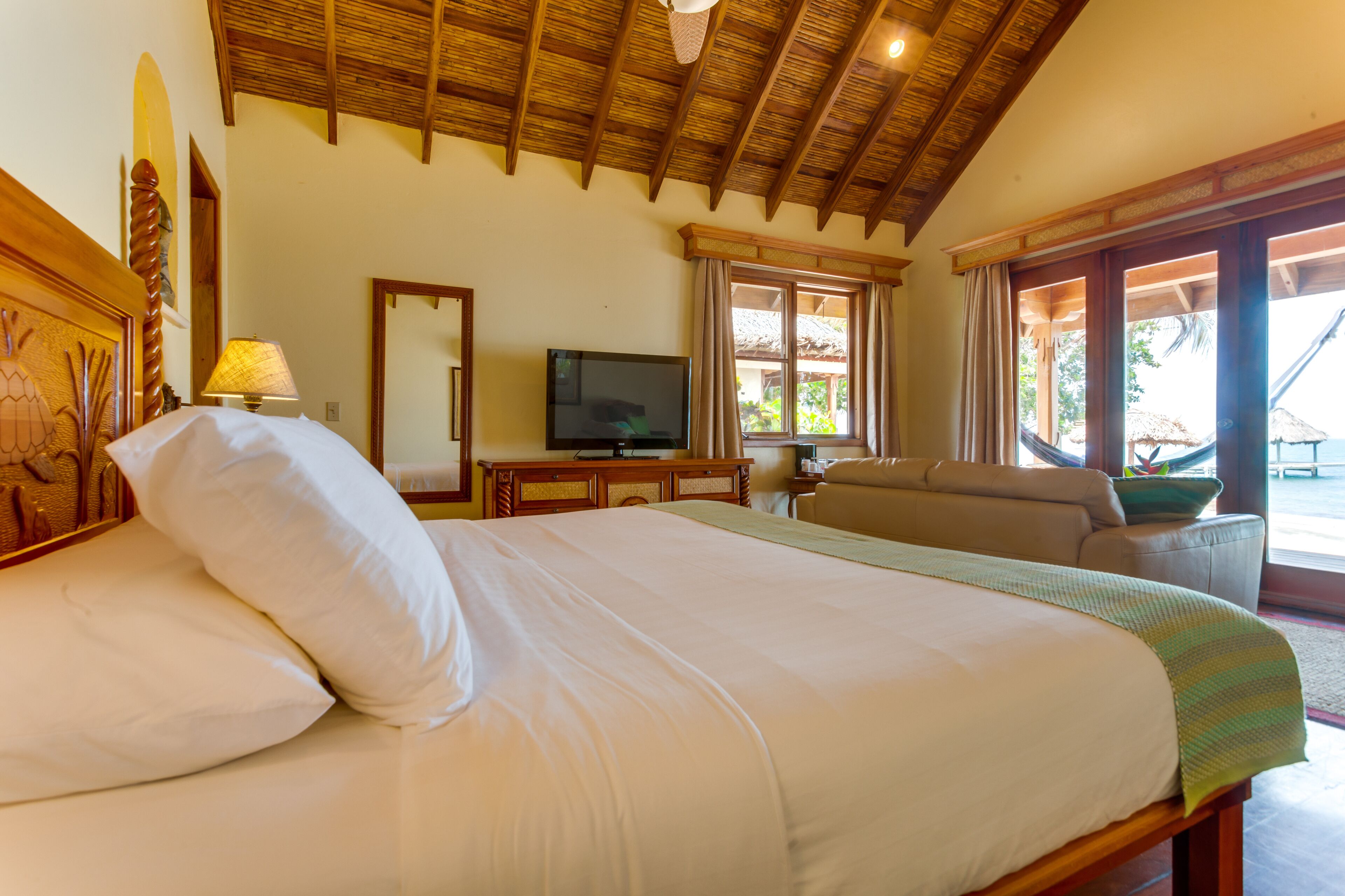 A hotel room with a large bed, a television, a sofa, and a window with curtains.
