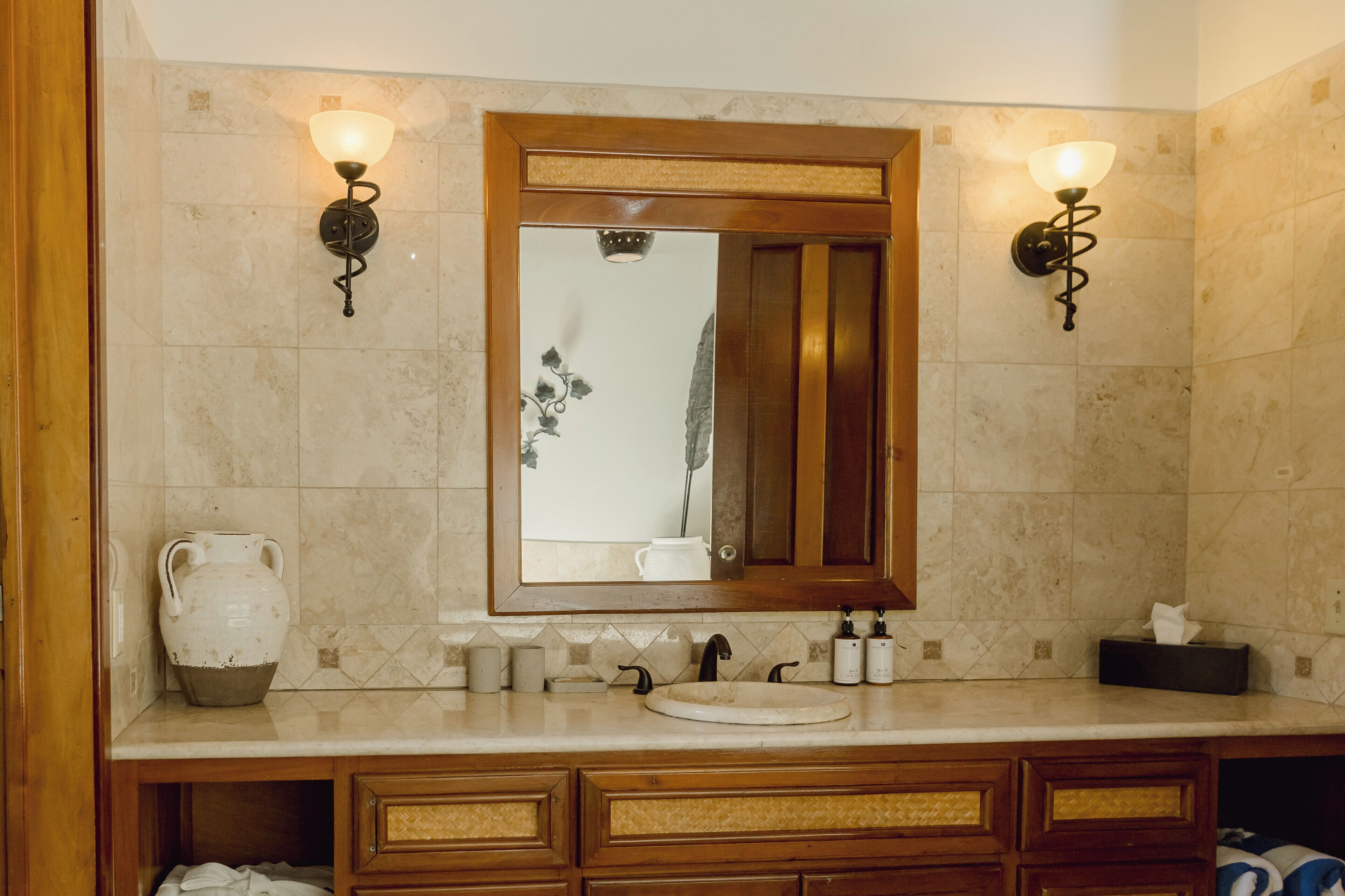 A bathroom with a large mirror, two wall-mounted lights, a sink, and a vanity with drawers.