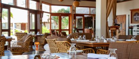 A restaurant with wooden tables, wicker chairs, and large windows.