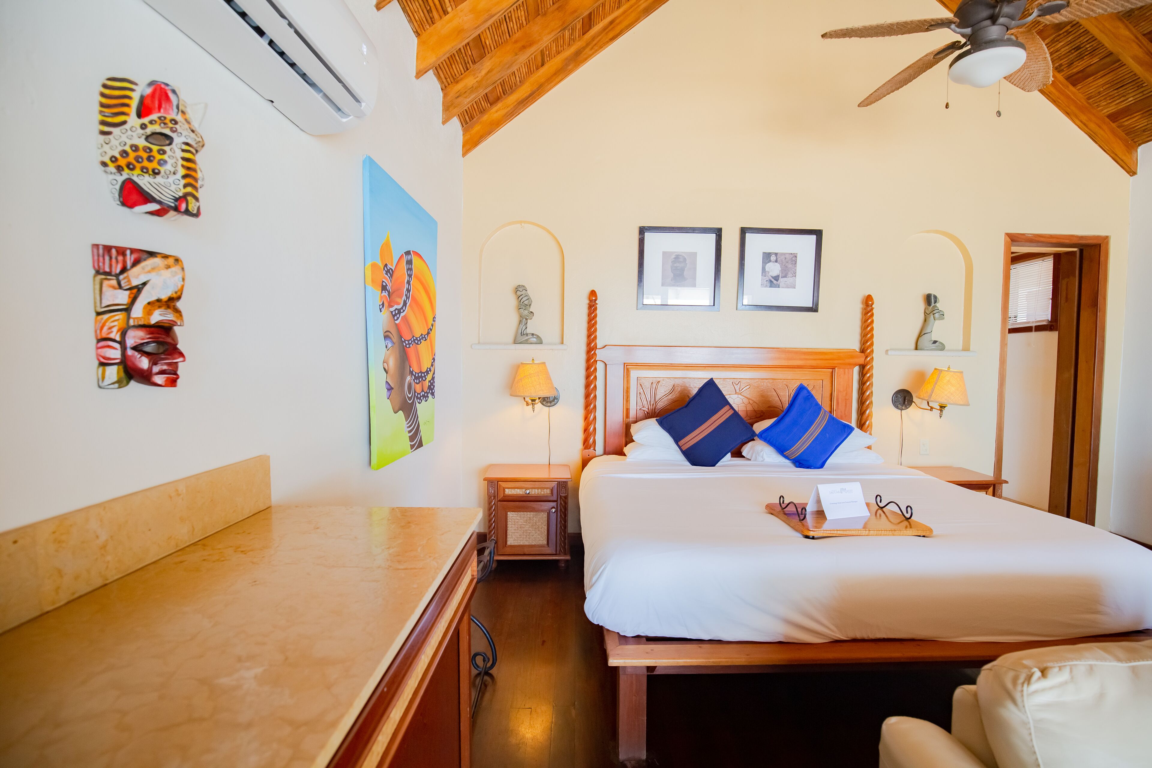 A hotel room with a wooden bed, two framed pictures, a ceiling fan, and wall art.