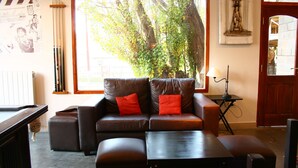 A cozy living room with a brown leather sofa, two red cushions, a wooden coffee table, and a billiards table. - Hotel Punta Norte (El Calafate)