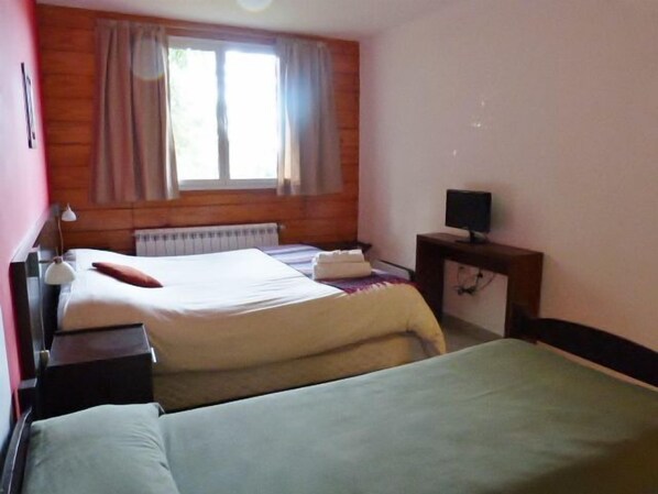 A room with two beds, a window with curtains, a desk with a computer, and a lamp.