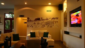 A hotel lobby with a reception desk, a white sofa with green cushions, a wall mural, and a television on the wall. - Hotel Punta Norte (El Calafate)