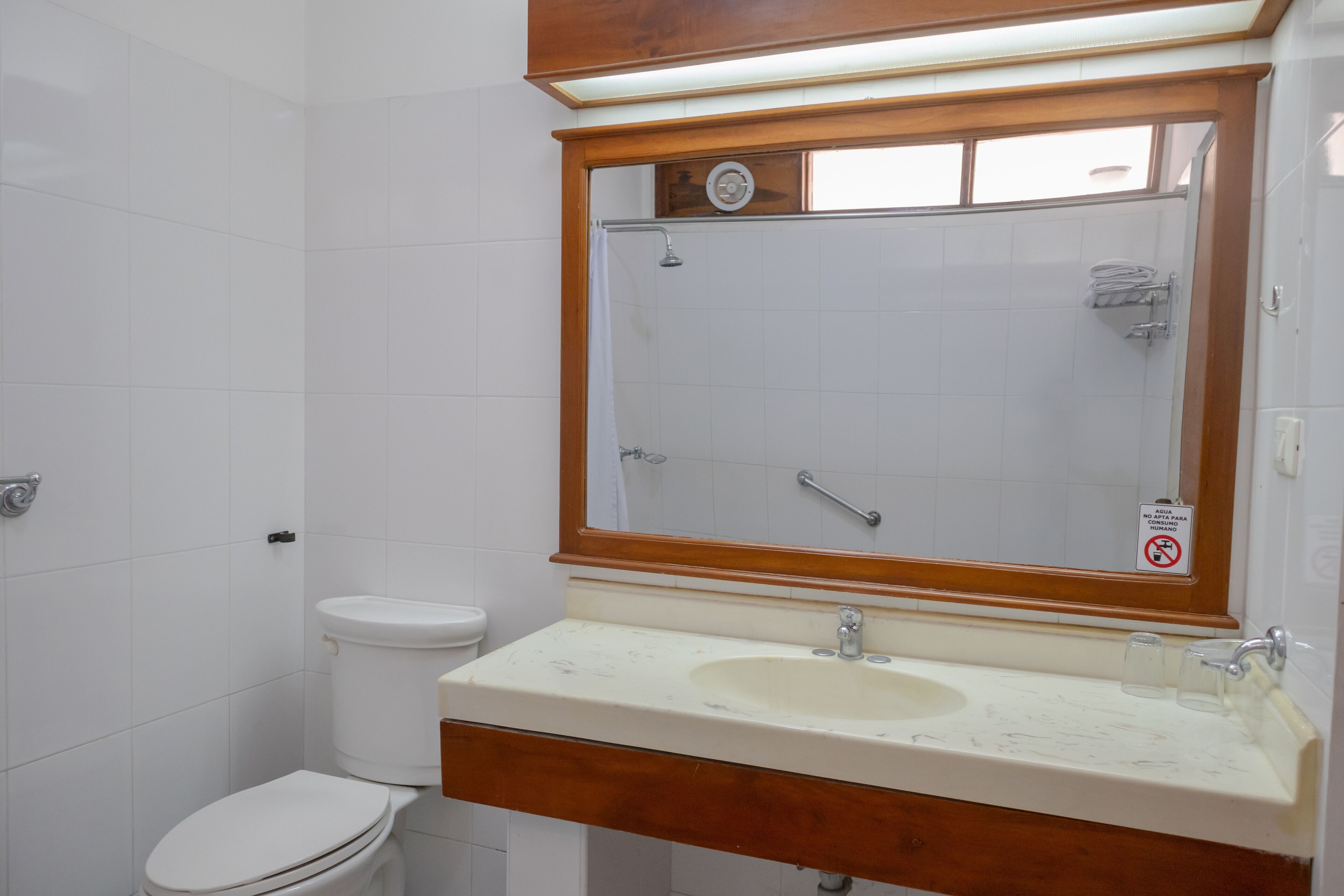 Une salle de bain avec des toilettes blanches, un lavabo et un miroir avec un cadre en bois.