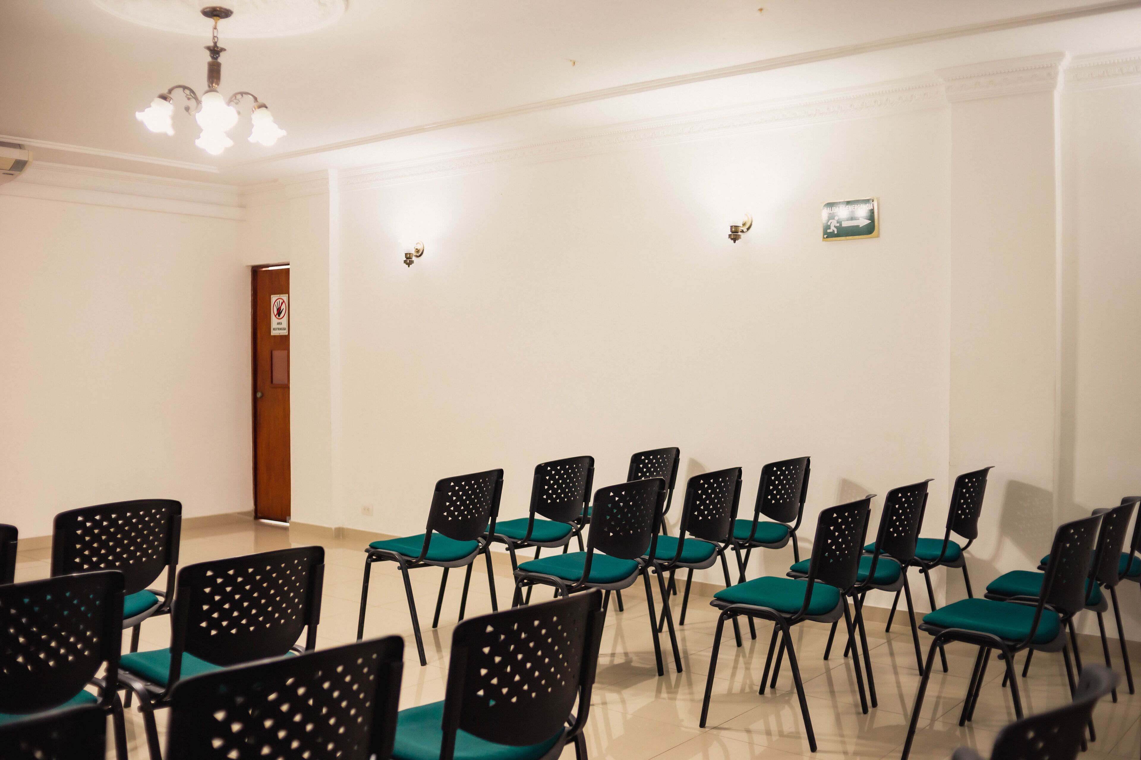 A conference room with rows of black chairs with green cushions, white walls, and a wooden door.