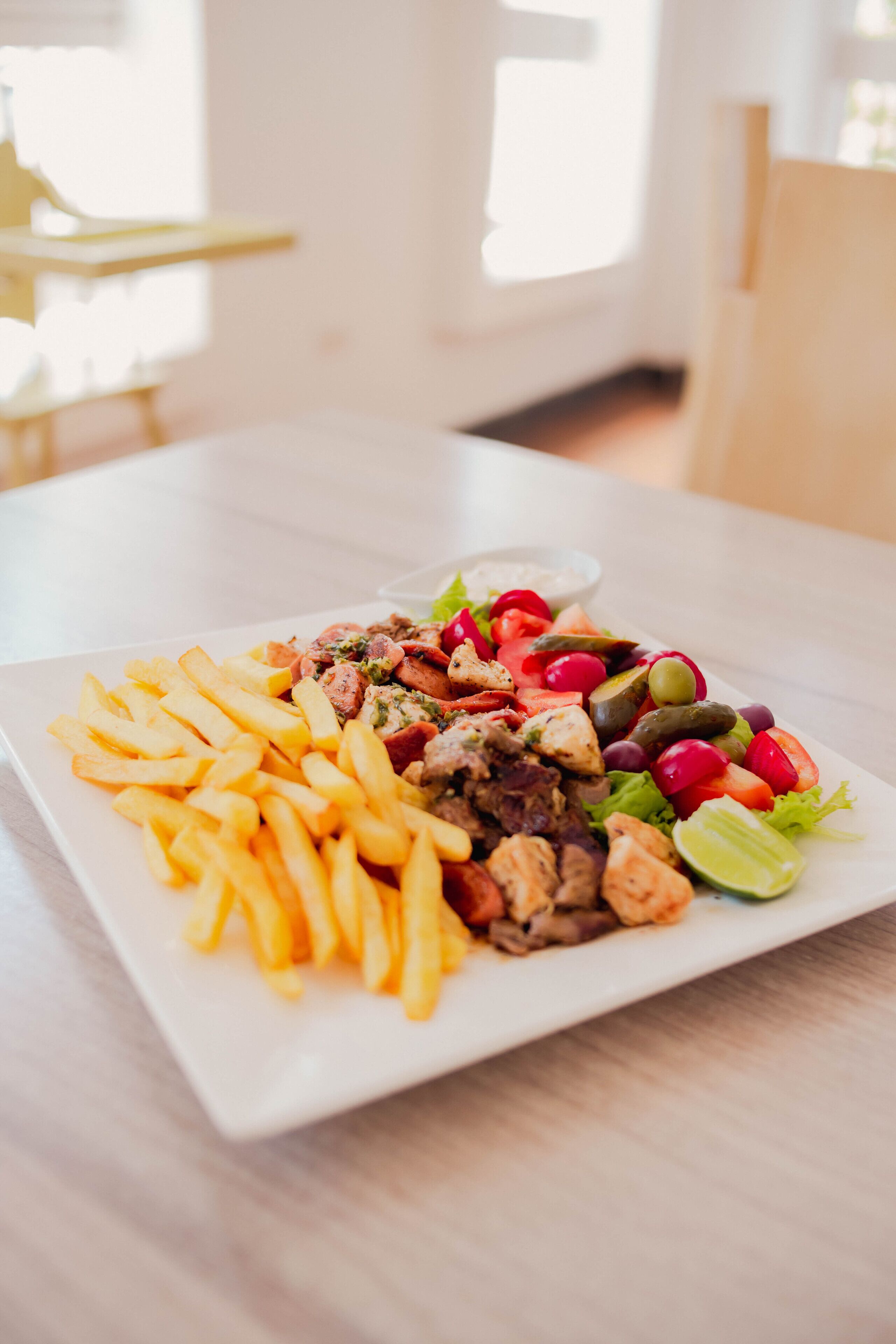 Un plato rectangular blanco con ensalada, carne a la parrilla y papas fritas.