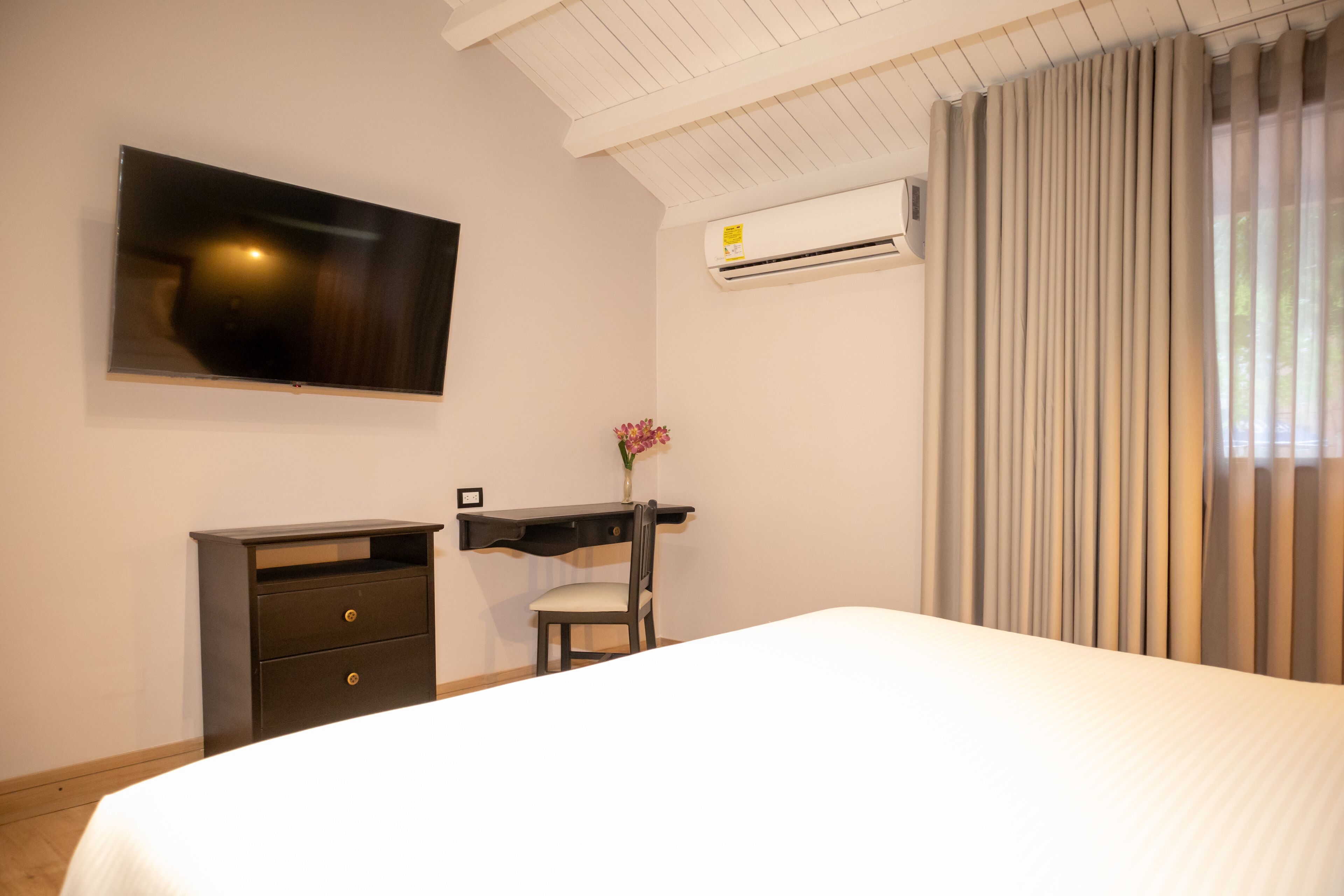 Ein Hotelzimmer mit Bett, Schreibtisch, Stuhl, Fernseher und Klimaanlage.