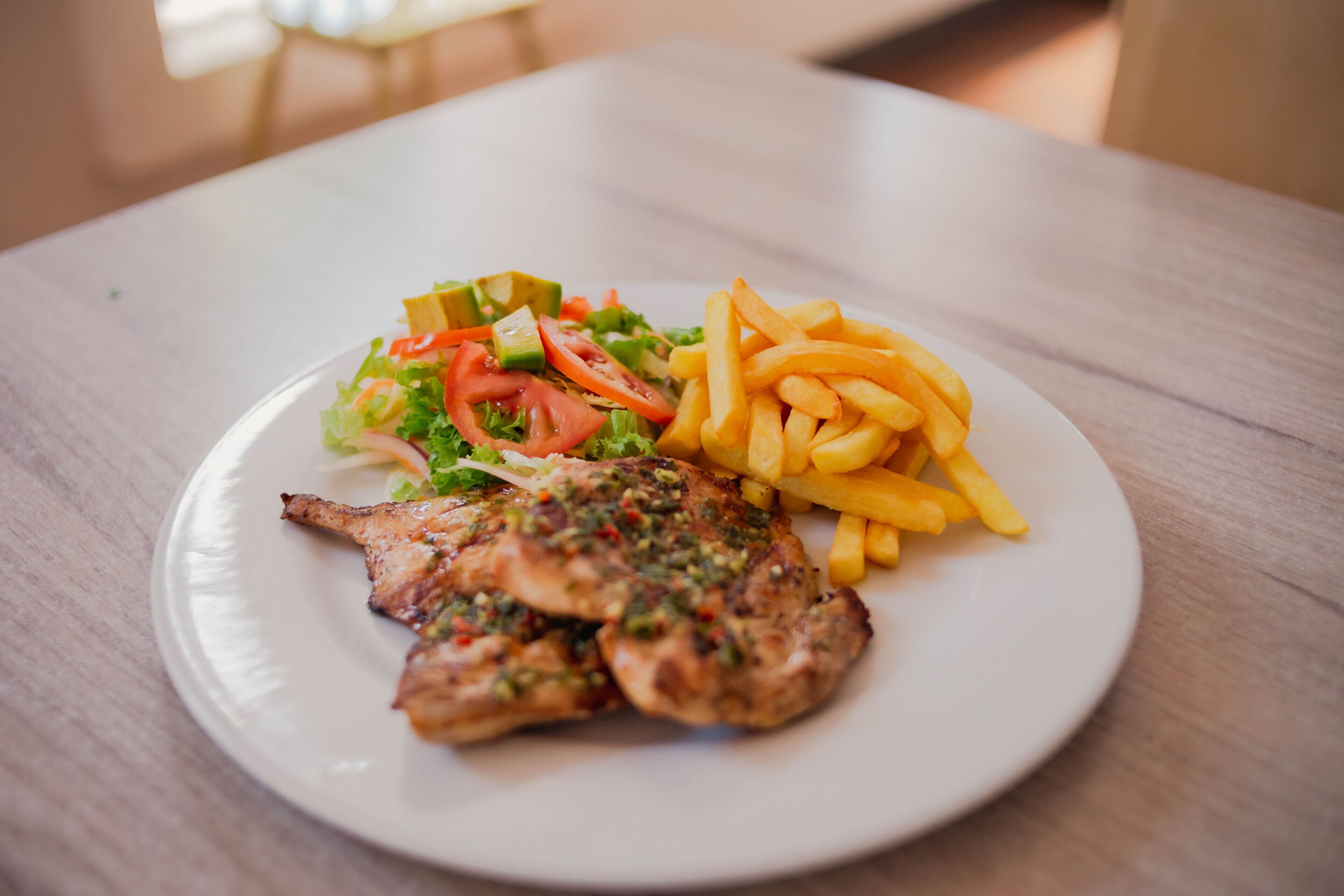 Un plato con pollo a la parrilla, una ensalada y papas fritas sobre un plato blanco.