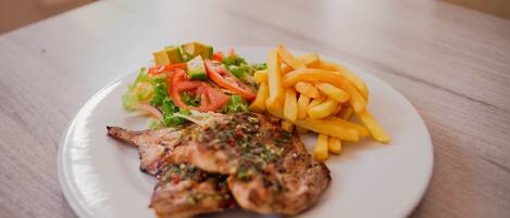 Un plato con pollo a la parrilla, una ensalada y papas fritas sobre un plato blanco.